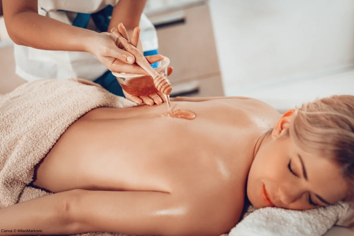 Mulher relaxando em uma mesa de spa enquanto recebe uma massagem com mel, destacando os benefícios do mel para a pele e o bem-estar.